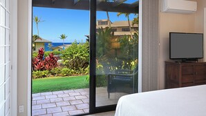 A hotel room with a sliding glass door leading to a balcony with a view of the ocean and palm trees.