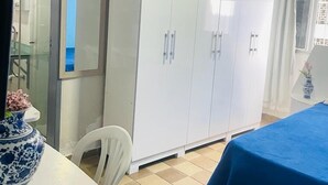 A room with a bed, a white wardrobe, a small table with a vase, and a ceiling fan. - Apto 701 em Boa Viagem  (Recife)