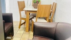 A small, clean room with a tiled floor, a wooden dining table with four chairs, a television mounted on the wall, and a brown leather sofa. - Apto 701 em Boa Viagem  (Recife)