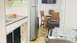 A compact kitchen with a refrigerator, a stove, and a dining area with chairs and a table. - Apto 701 em Boa Viagem  (Recife)