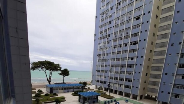 A swimming pool with a slide, surrounded by a landscaped area with trees and a view of the beach. - Apto 701 em Boa Viagem  (Recife)