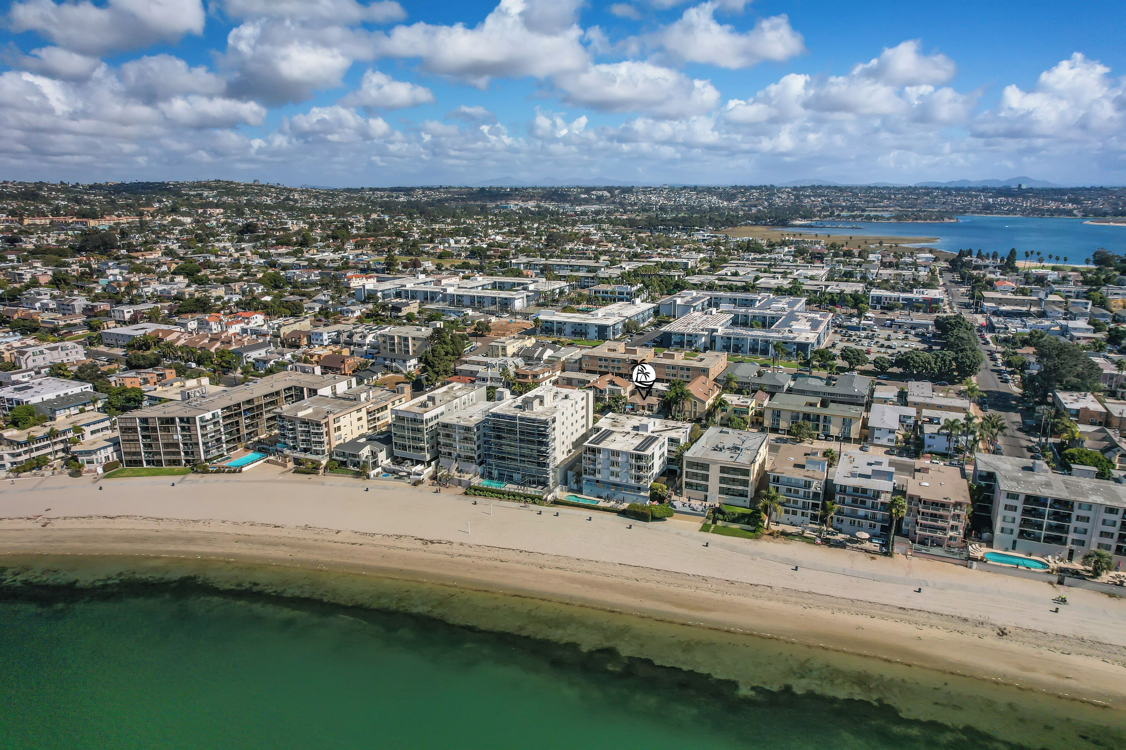 Una vista aerea di una zona residenziale costiera con edifici moderni, una spiaggia e una vasta distesa d'acqua.