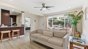 A modern living room with a beige sofa, wooden stools, a glass coffee table, and a ceiling fan. - La Jolla Dream! Amazing Location - Large Patio, Fire Pit and Parking! (La Jolla)