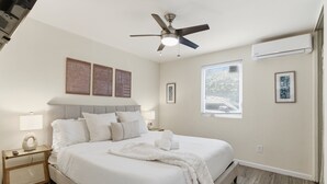 A neatly arranged bedroom with a bed, bedside tables, a ceiling fan, and wall-mounted air conditioning. - La Jolla Dream! Amazing Location - Large Patio, Fire Pit and Parking! (La Jolla)