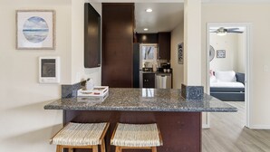 A kitchen with a granite countertop, two woven stools, a framed picture, and a ceiling fan in the adjacent room. - La Jolla Dream! Amazing Location - Large Patio, Fire Pit and Parking! (La Jolla)