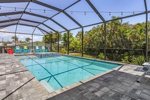 Une piscine dotée d’un patio couvert, entourée de palmiers et avec une maison en arrière-plan.