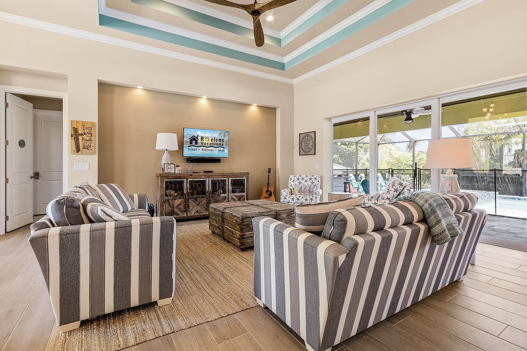 A spacious living room with striped sofas, a television, and a large window offering a view of the outdoors.