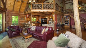 Ein großzügiges Blockhaus-Interieur mit hoher Decke, einer zentralen Sitzecke mit Ledersofas, einem Essbereich und einer Küche.