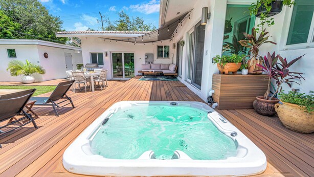 Een houten terras met een jacuzzi, tuinmeubilair en plantenpotten.