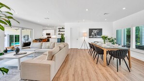 Een moderne woonkamer met een bank, een eettafel en stoelen. Er staat een lamp, een plant en er hangt een schilderij aan de muur.