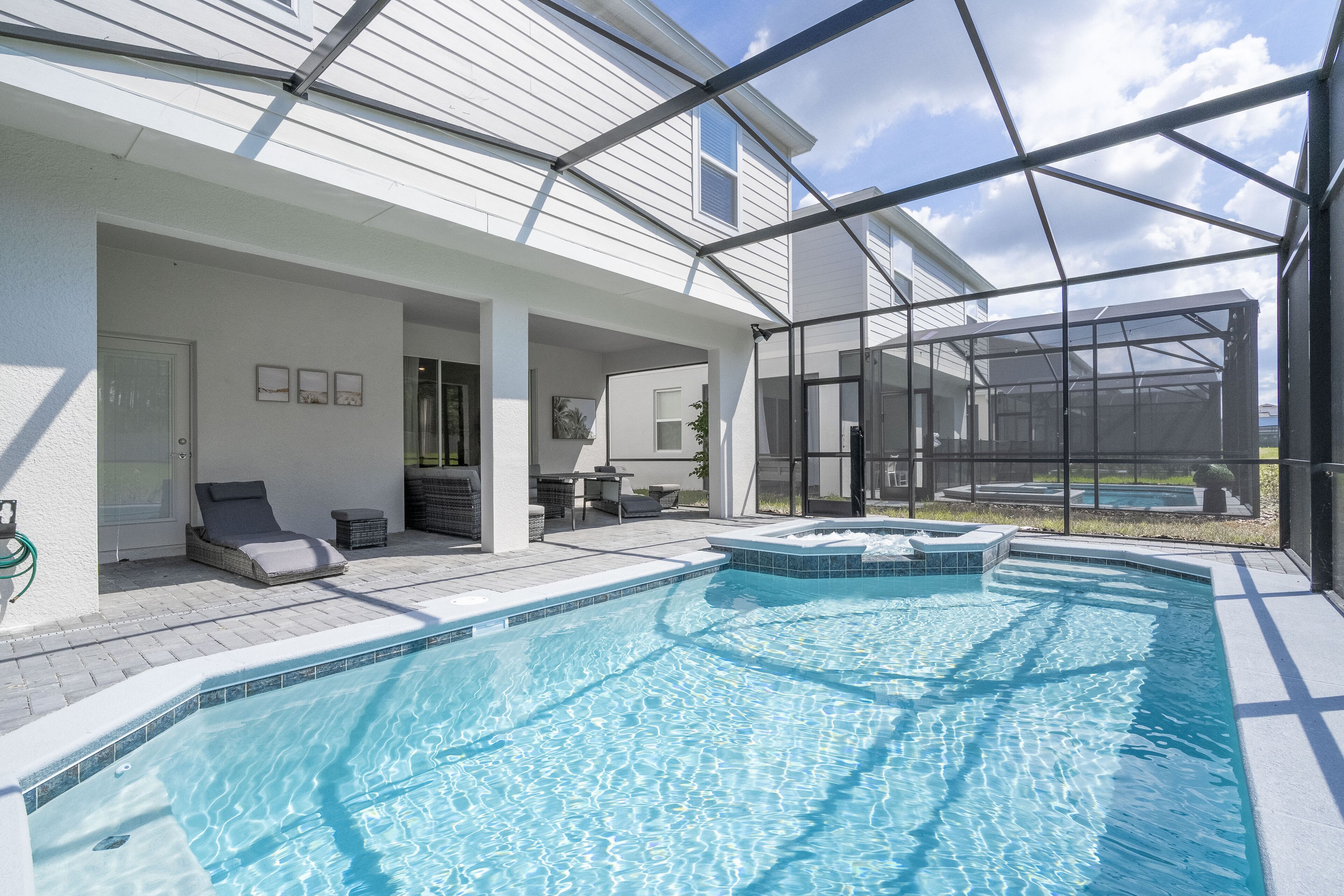 A swimming pool with a glass enclosure, a covered patio area with seating, and a view of the backyard.