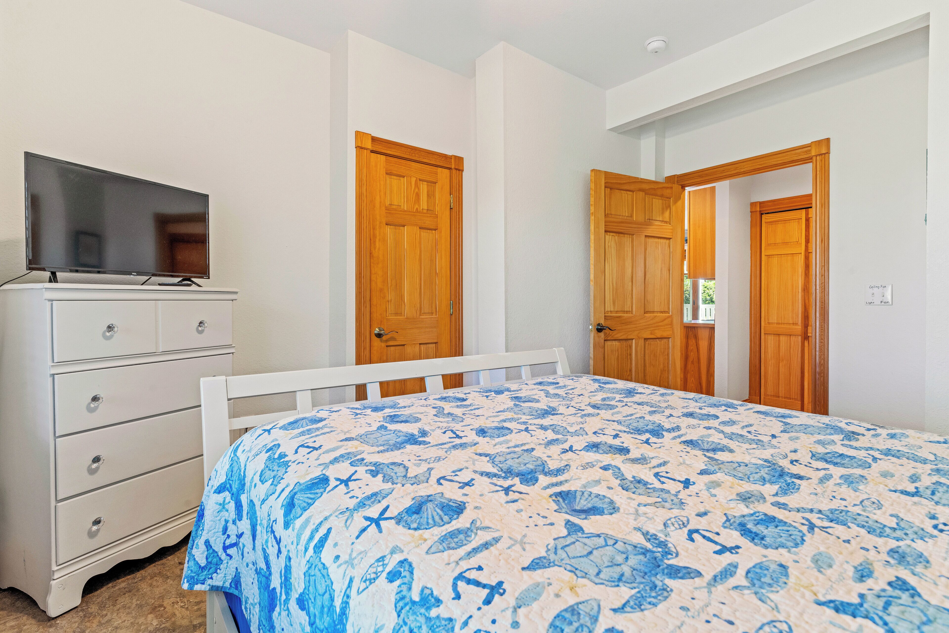 A bedroom with a bed, a dresser, a television, and wooden doors.