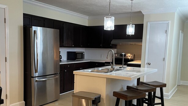 A modern kitchen with a stainless steel refrigerator, a microwave, a sink, and a bar area with stools.