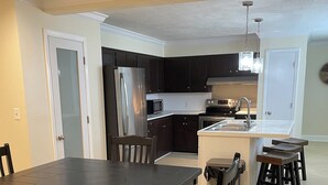 A modern kitchen with dark cabinetry, a central island with a sink, and a dining area with a large table and chairs.