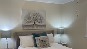A bedroom with a large bed, two bedside tables with lamps, a ceiling fan, and a wall-mounted painting.