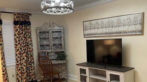 A living room with a TV on a wooden stand, a patterned rug, a wooden cabinet, and a ceiling light.