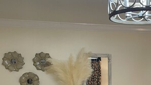 A room with a light wooden console table, three wall-mounted decorative mirrors, and a vase with pampas grass.