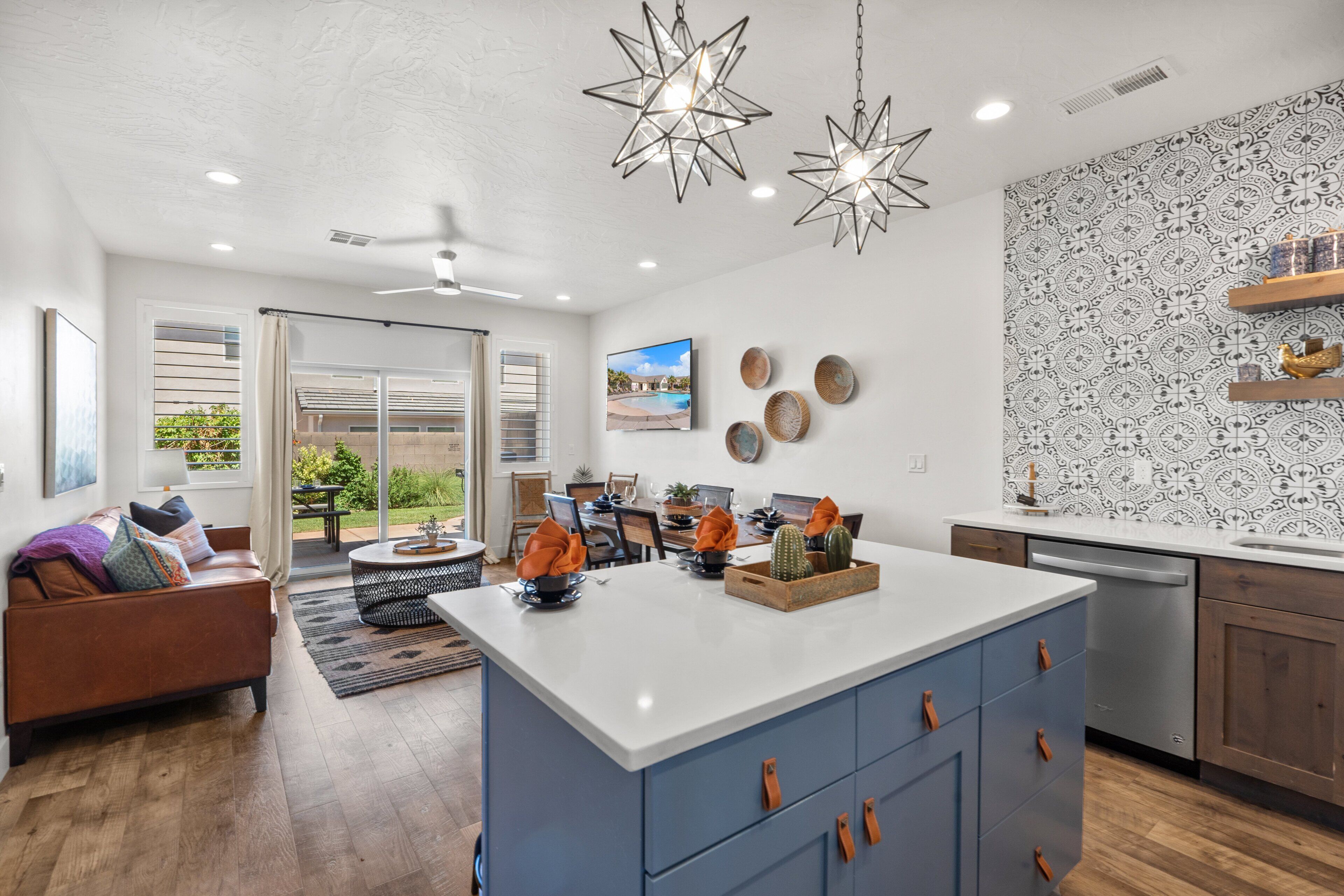 A modern kitchen with a central island, a dining area with a view of the outdoors, and a living room with a sofa and a coffee table.