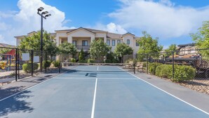 A tennis court with a net, surrounded by a fence, and a building with multiple windows in the background. - Freedom Village Retreat, Neighboring units, Near St George (Washington)