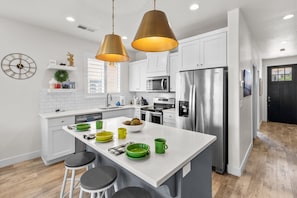 A modern kitchen with white cabinetry, stainless steel appliances, and a central island with stools.
