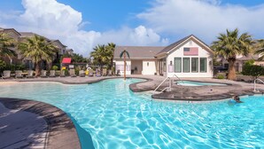 A swimming pool with a small building featuring an American flag, surrounded by palm trees and lounge chairs. - Freedom Village Retreat, Neighboring units, Near St George (Washington)