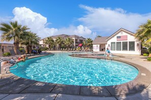 A swimming pool with a clear blue water, surrounded by palm trees and a building with an American flag. - Freedom Village Retreat, Neighboring units, Near St George (Washington)