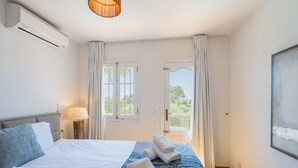 Ett hotellrum med en säng, en lampa, ett fönster med gardiner och en luftkonditioneringsanläggning.