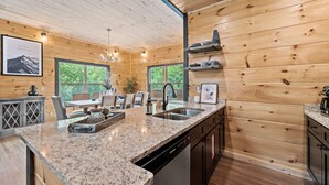 Cocina con encimeras de granito, gabinetes de madera y lavavajillas. Se observa una ventana con vistas a zonas verdes.