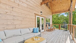 Una terraza de madera con sofá y sillones, un sillón colgante y un espacio cubierto con luces de cuerda.