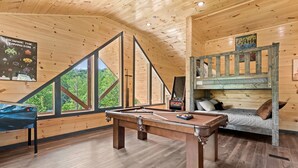 Interior de madera con mesa de billar, literas y vista a la vegetación.