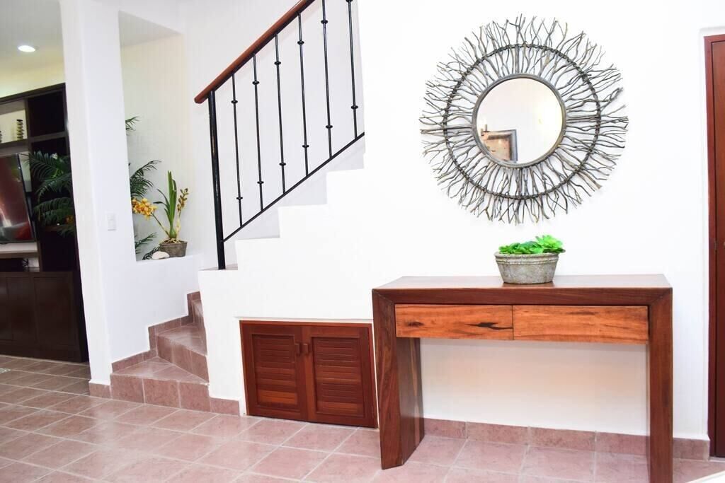 A staircase with a wooden handrail and a metal railing, a wooden console table with a potted plant, and a wall-mounted mirror with a sunburst design.