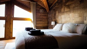 A wooden cabin-style bedroom with a large bed, a window, and a stone wall. - Chalet Kusi Wasi is a luxury home in the heart of the pyrénées mountains  (Font-Romeu-Odeillo-Via)