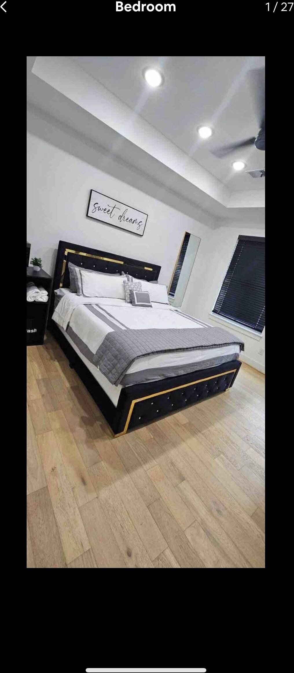 A bedroom with a bed, a nightstand, a wall-mounted light, and a window with blinds.