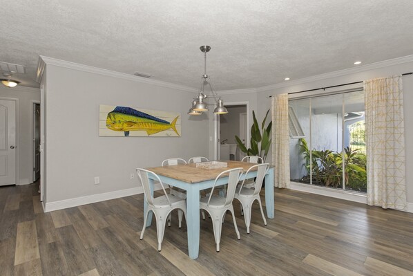 A dining area with a light blue table and white chairs, a ceiling light fixture, and a large fish painting on the wall.