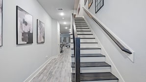 A modern interior with a staircase, white walls, and framed artwork. - Modern 2024 Mansion with Indoor Basketball, Huge TVs & Near Downtown (Houston)