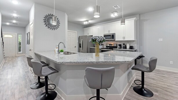 A modern kitchen with a central island, bar stools, and pendant lighting. - Modern 2024 Mansion with Indoor Basketball, Huge TVs & Near Downtown (Houston)
