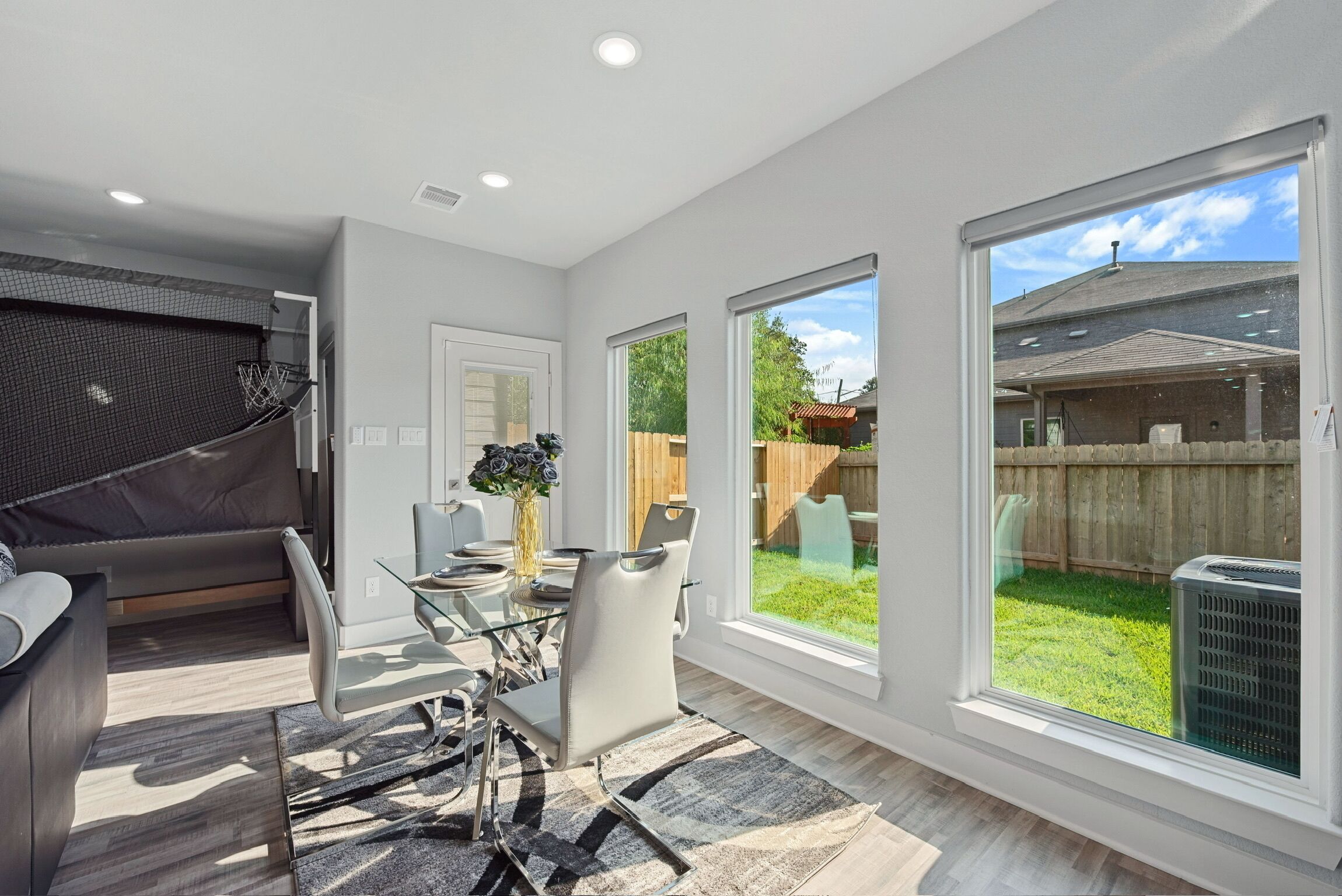 A modern kitchen with a dining area, large windows, and a view of the backyard.