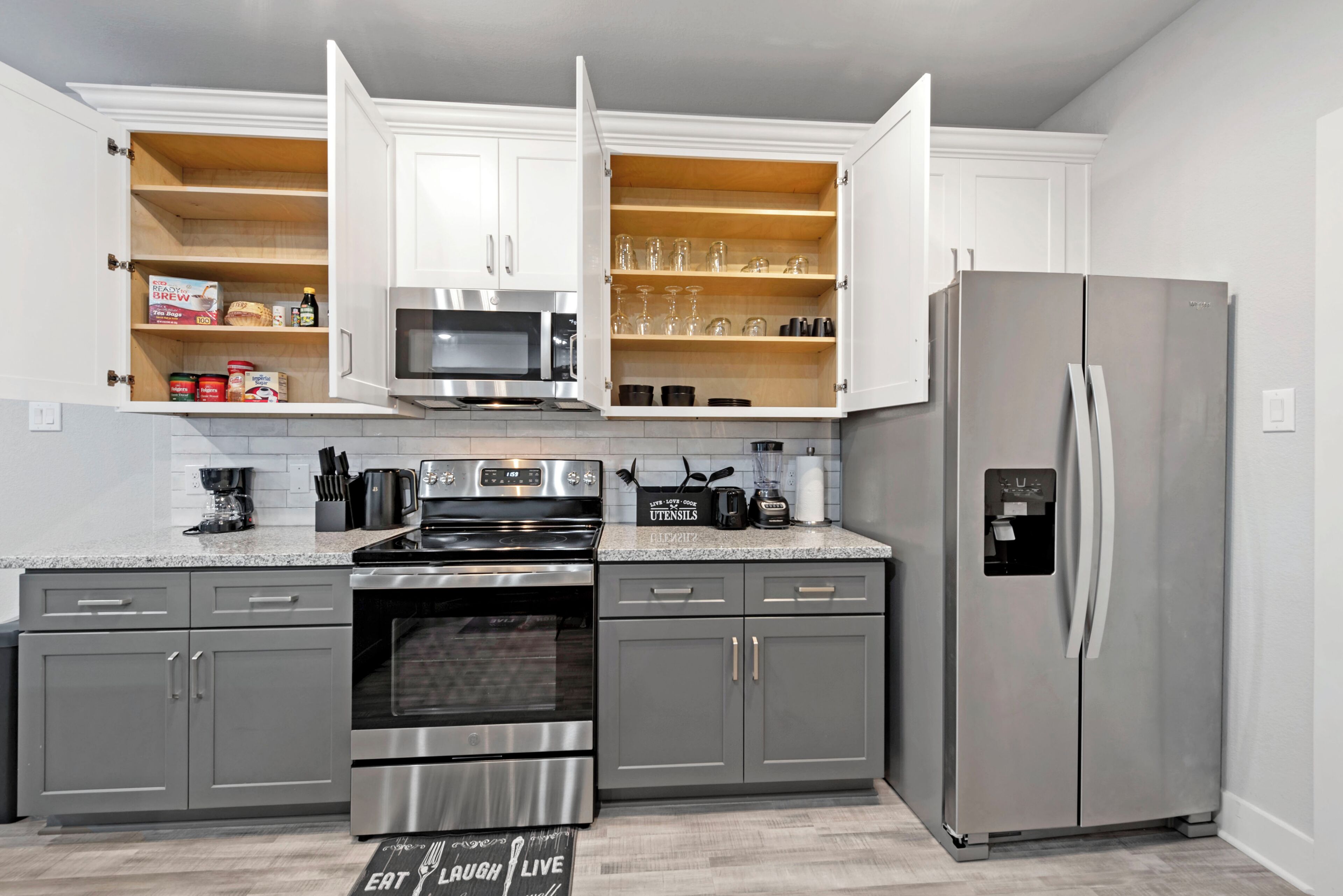 A modern kitchen with white cabinets, stainless steel appliances, and open shelving.