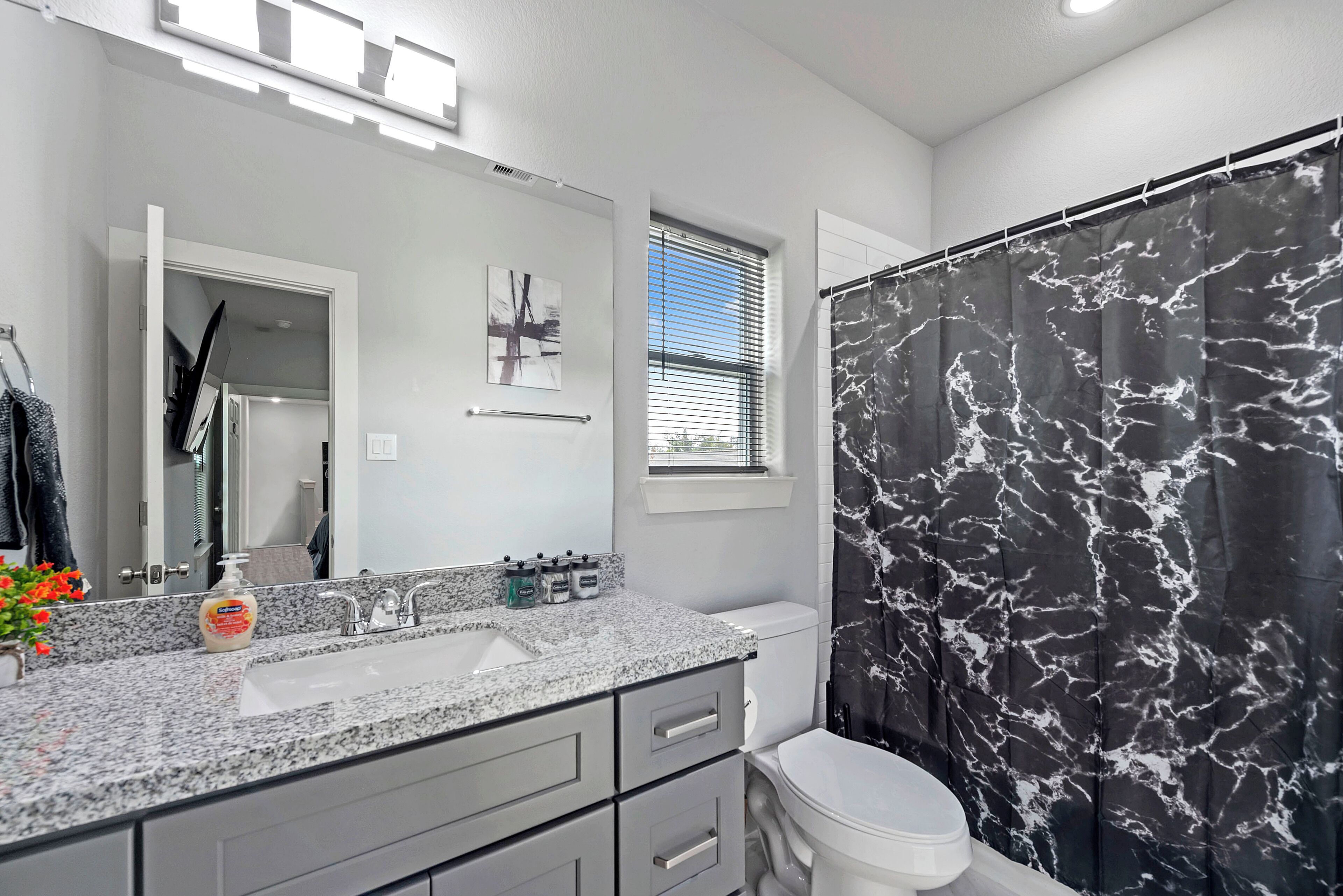 A bathroom with a marble shower curtain, a sink with a mirror, and a toilet.