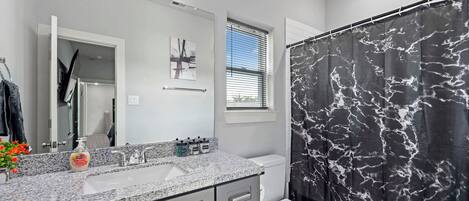 A bathroom with a marble shower curtain, a sink with a mirror, and a toilet.