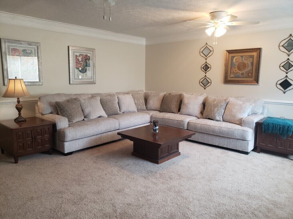 A living room with a beige sectional sofa, a dark wooden coffee table, and a ceiling fan.
