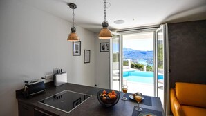 A modern kitchen with a central island, a dining area with a view of a pool and mountains, and a yellow leather chair.
