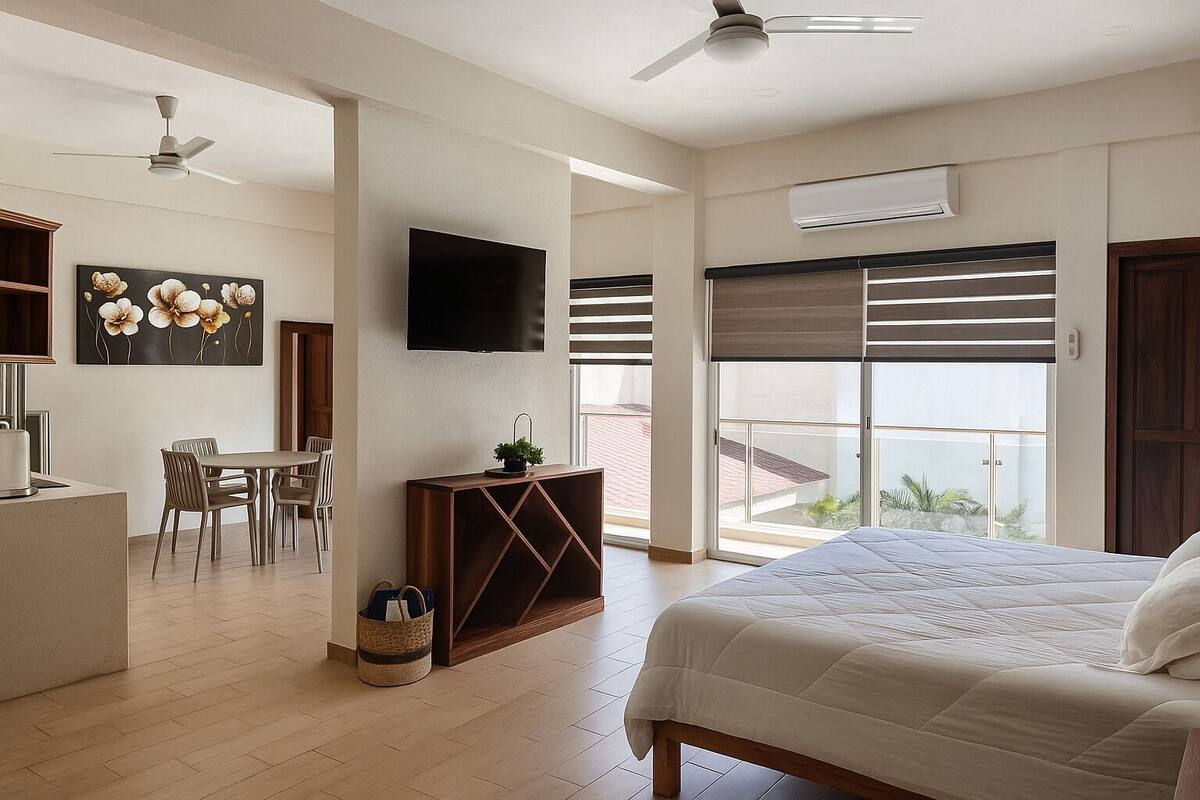 A modern hotel room with a bed, a desk, a chair, a TV, and a balcony with a view.