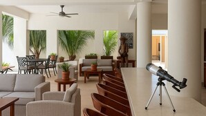 A modern indoor space with a long wooden bar, seating area with sofas and chairs, ceiling fans, and potted plants. - Casa Boutique Maria Bonita  (La Manzanilla)