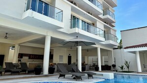 A modern multi-story building with a swimming pool, outdoor seating, and a balcony with glass railings. - Casa Boutique Maria Bonita  (La Manzanilla)