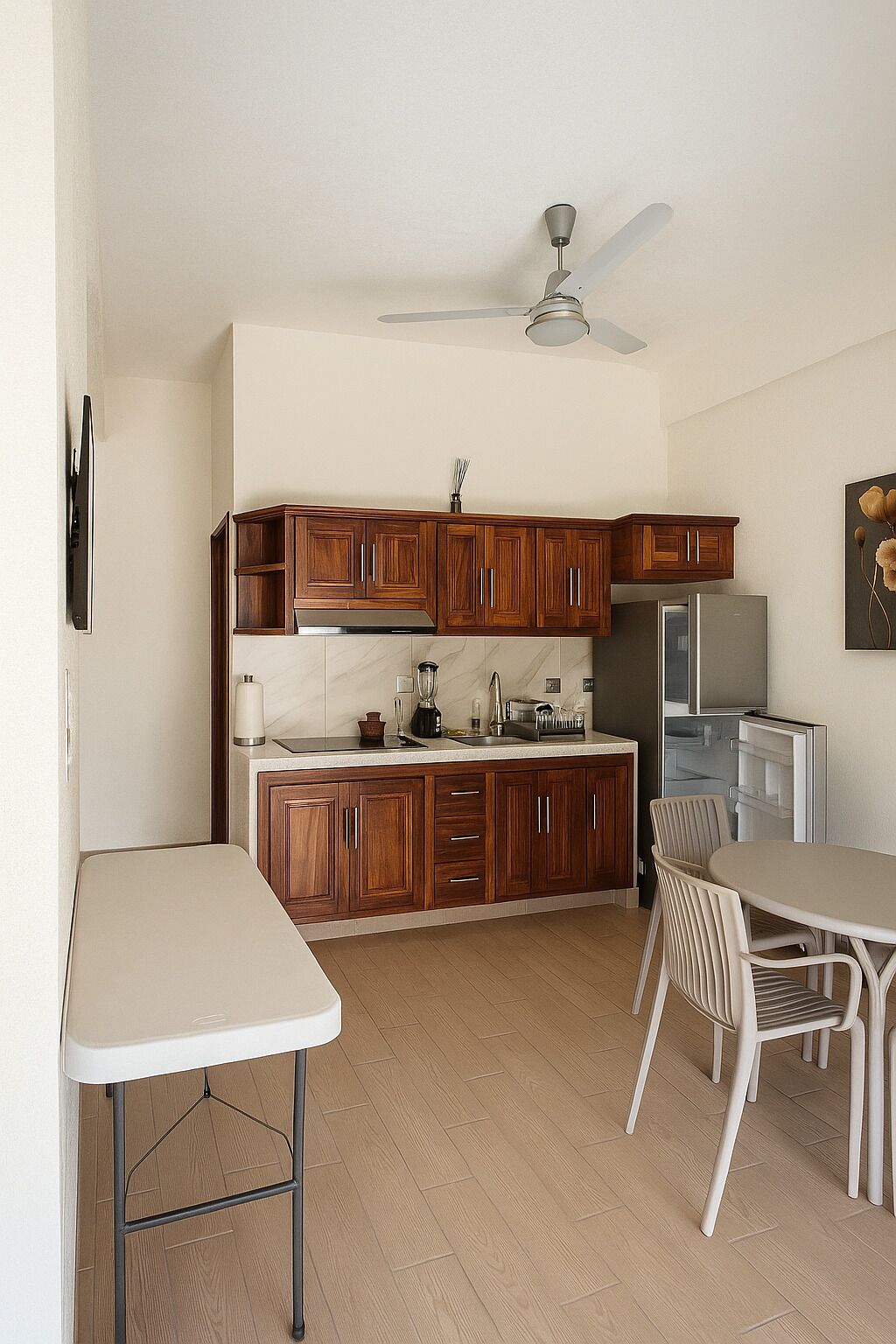 Una cocina compacta con armarios de madera, estufa integrada y un refrigerador. Hay una mesa de comedor con sillas y un ventilador de techo.