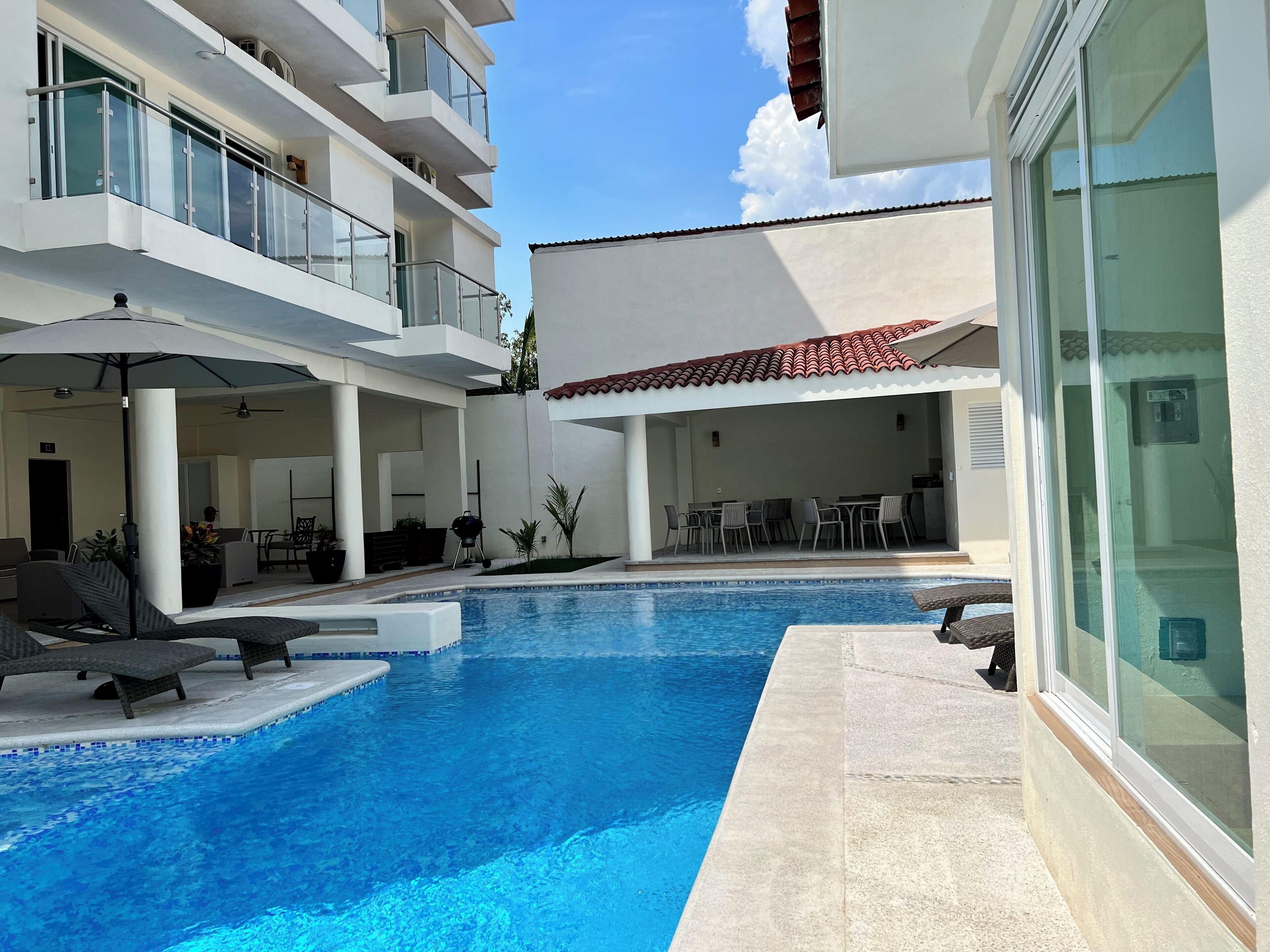 A modern hotel with a swimming pool, outdoor seating, and a covered patio area.