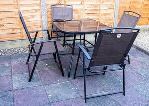 Un patio con una mesa de vidrio y cuatro sillas con estructura metálica y respaldo de malla.