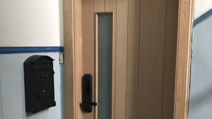 Uma porta de madeira com um painel de vidro vertical e uma maçaneta preta.