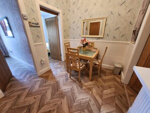 A dining area with a wooden herringbone floor, a glass-top table, and wooden chairs. A mirror hangs on the wall above the table. - Apartment - Largs - Sleeps 4 - Pet Friendly (Largs)